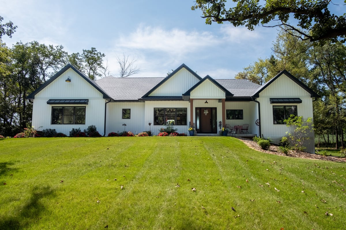 Modern white ranch house with multiple gabled roofs and large windows set on a green lawn surrounded by trees