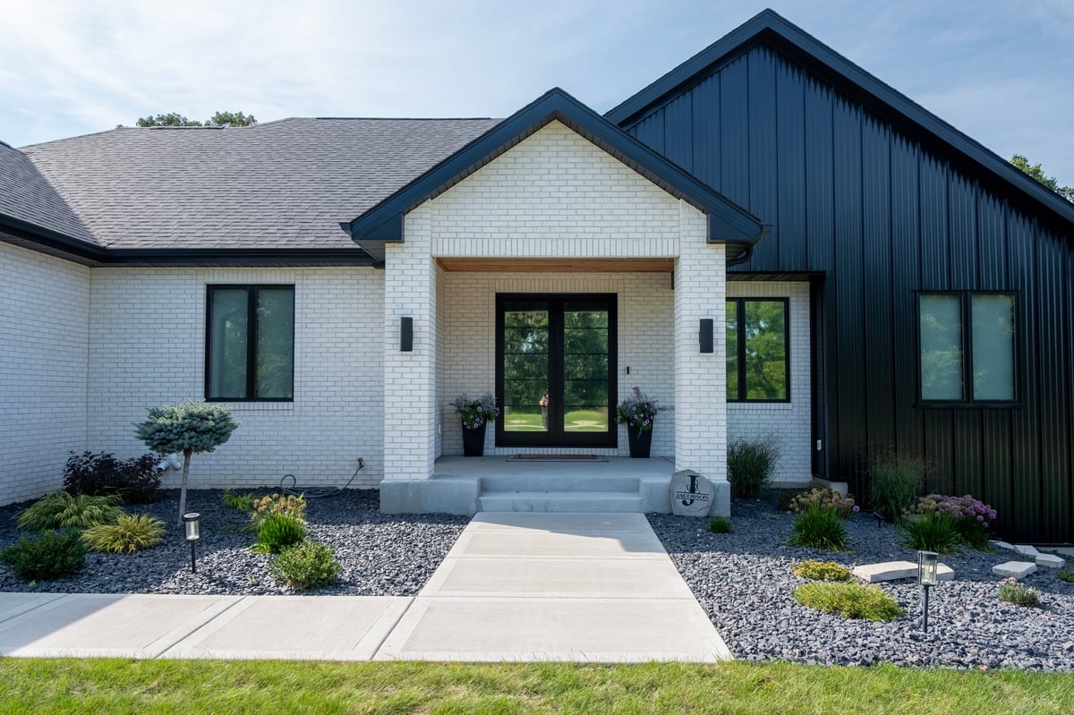 Modern home exterior with white and black siding, central entrance, concrete walkway, and contemporary landscaping design