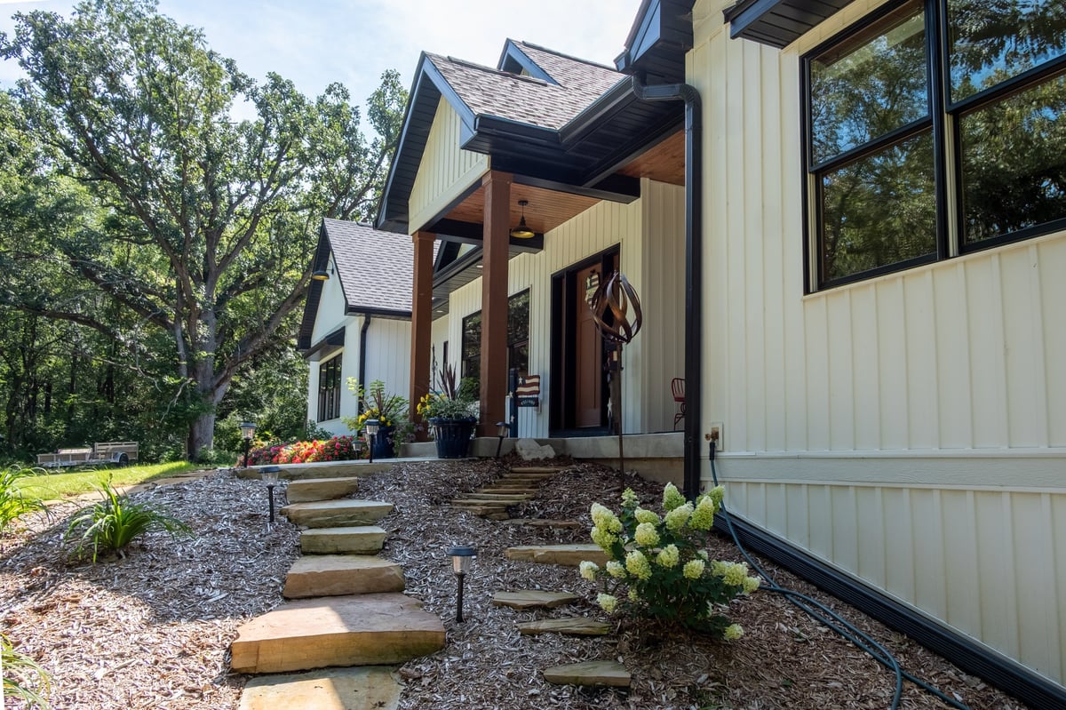 Modern farmhouse with white metal siding, covered porch, and stone pathway entrance surrounded by landscaping