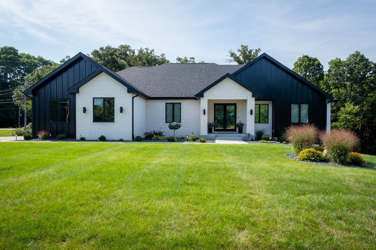 Modern farmhouse with black and white exterior, multiple gabled roofs, and manicured lawn surrounded by trees